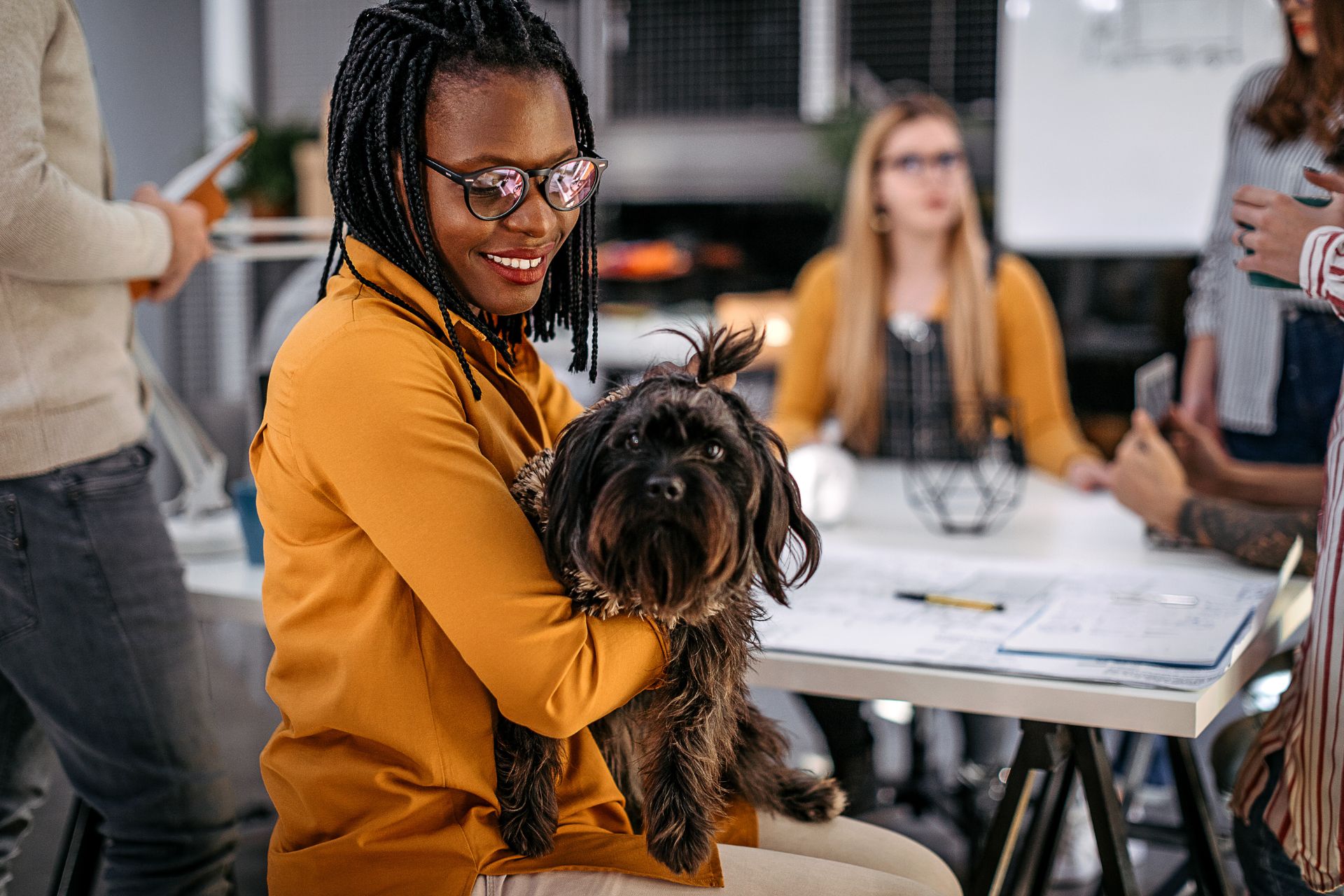 A woman holds a pet dog while her colleagues are working in the background