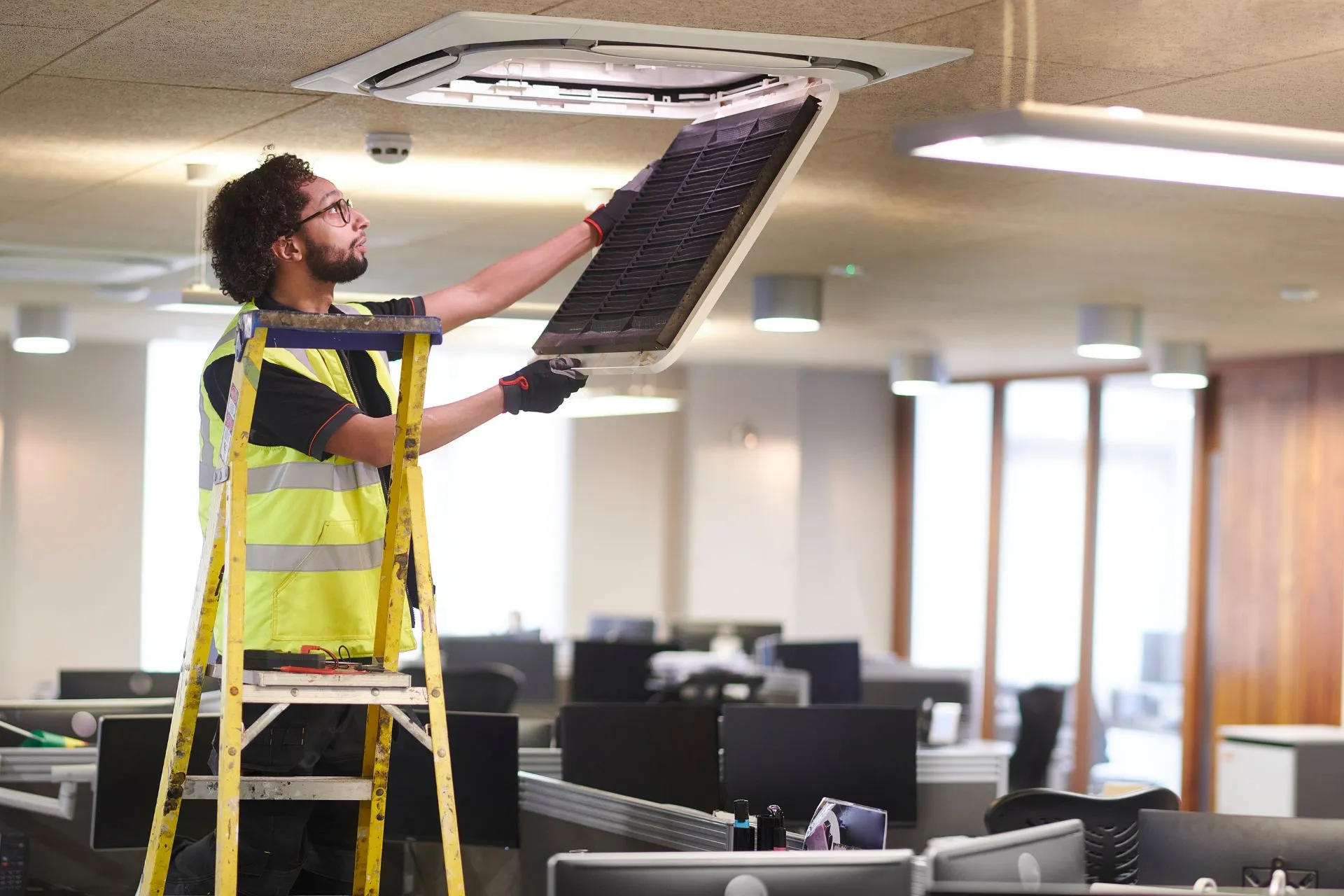 Maintenance engineer on a ladder servicing an office ceiling unit
